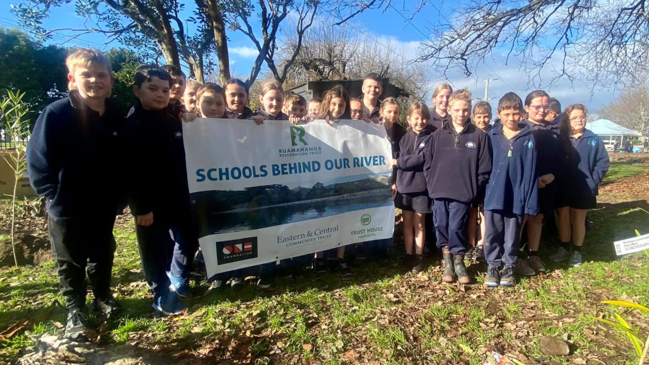 A group of school children with a "Schools Behind Our River" banner